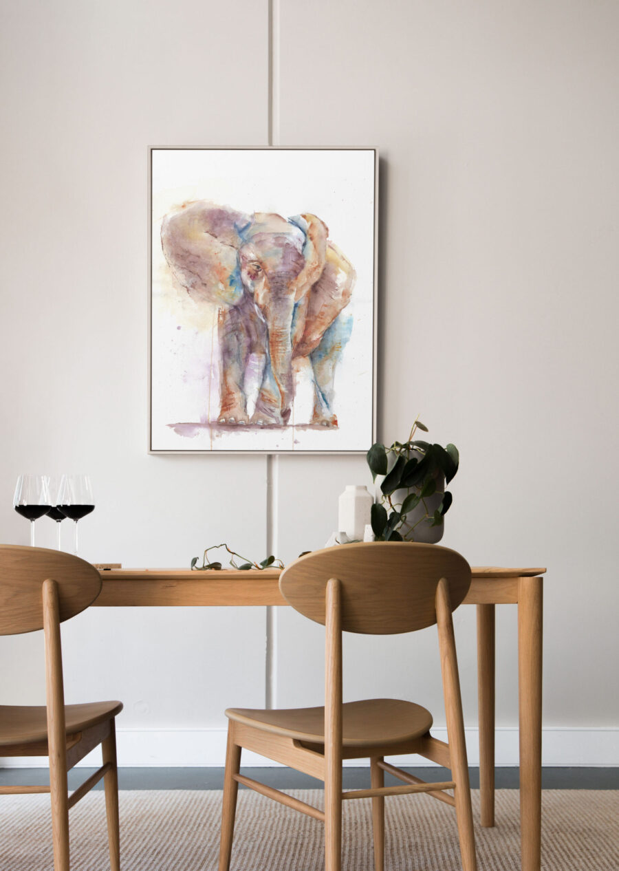 Cuadro enmarcado con una acuarela de un elefante, decorando un comedor minimalista con muebles de madera.